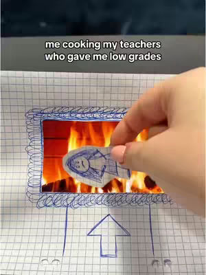 The image shows a hand holding a drawing of a person over what appears to be a paper-based, drawn fireplace with flames. The text overlayed on the top says: 'me cooking my teachers who gave me low grades'. The drawing of the person features a sad face, suggesting a playful portrayal of revenge.