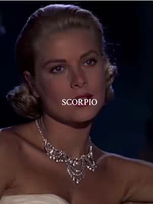 A close-up shot featuring a well-lit woman with blonde hair styled in an updo. She wears a diamond necklace. The word "SCORPIO" is overlaid on the image in white text.