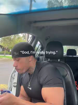 A man is sitting in the driver's seat of a car. The text overlay reads "God, I'm really trying."