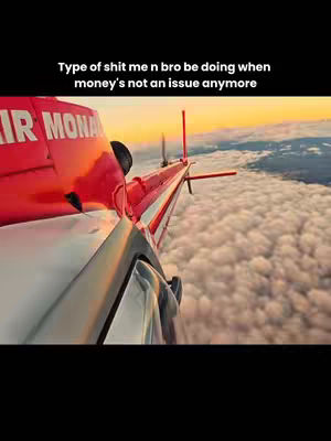 The cover image shows the perspective from within a red and silver aircraft, likely a helicopter, flying above a sea of clouds. The image is shot from a low angle, looking up towards the horizon. The aircraft's tail, bearing the text 'AIR MONA' is prominently visible. Above this is a black bar with white text that states a lighthearted theme about wealth. The sky is colored with the warm hues of a sunset.
