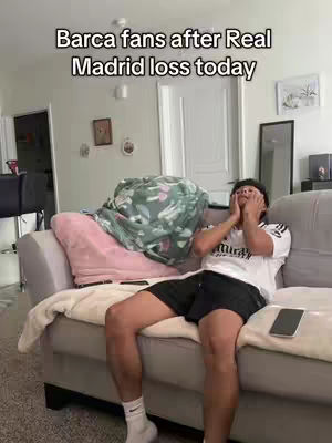 The cover image shows a young man sitting on a gray couch in a living room. He is wearing a white t-shirt and black shorts, and covering his face with his hands.  A soft, patterned blanket is draped over the back of the couch. The background includes white walls, a door, and some frames.
