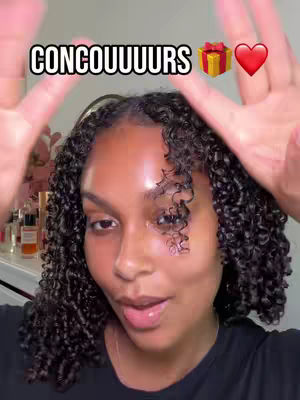 A woman with curly hair and a dark top has her hands up with the peace sign, framed by the caption "CONCOUURS", a gift box, and a heart emoji. The background reveals a well-lit room with objects on a shelf.