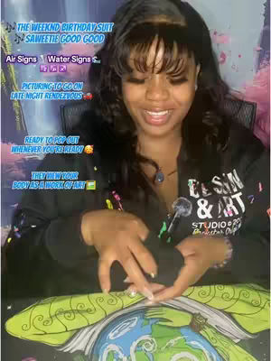 A woman with long dark hair and a black top is looking at the camera and smiling. She is appearing in front of a colorful background with text bubbles and a tarot card with the image of the earth with a world map. There is overlay text around her and she is holding something at the point of her stomach.