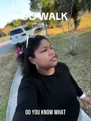 A person is walking towards the camera on a sidewalk, with cars parked on the street behind them. The person holds the camera and is looking up slightly. White text is added to the image.