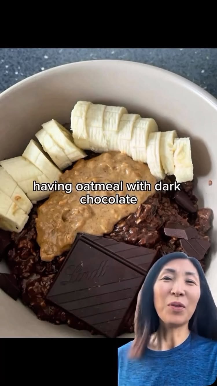 A medium shot of a woman in a blue shirt, looking directly at the camera, overlaid on a bowl of oatmeal with peanut butter, bananas and dark chocolate. The text overlay says 'having oatmeal with dark chocolate'.