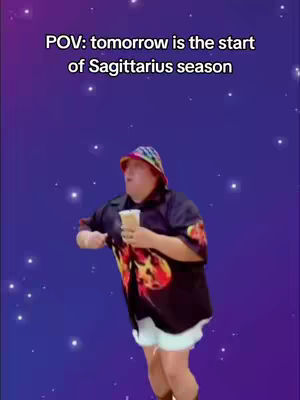 A man wearing a colorful hat and a black shirt with red flame-like patterns on it is dancing across a purple background filled with white stars. He holds a cup in one hand and wears white shorts and brown boots.