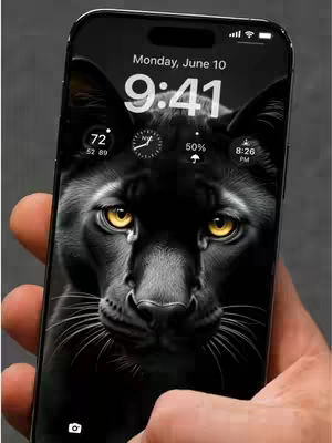 A hand holding a black smartphone displaying a close-up image of a black panther's face. The panther dominates the screen with its piercing yellow eyes and detailed fur. The screen also shows the time, date, and battery information, indicating it's the lock screen of the phone.