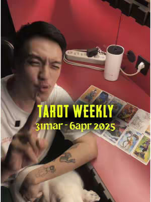 The cover image features an Asian man in a white t-shirt, pointing his index finger towards the viewer, possibly explaining or highlighting something. The background is a rich maroon or red, which contrasts with the man's fair skin and the white of his shirt and a white, cylindrical item. The text overlay in yellow and green on the screen reads "TAROT WEEKLY" and the time frame, 31mar - 6apr 2025.