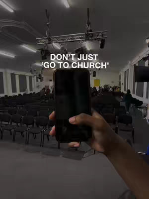 A person is holding a phone in front of a large auditorium with rows of black seating. The text overlay reads: DON'T JUST 'GO TO CHURCH'.