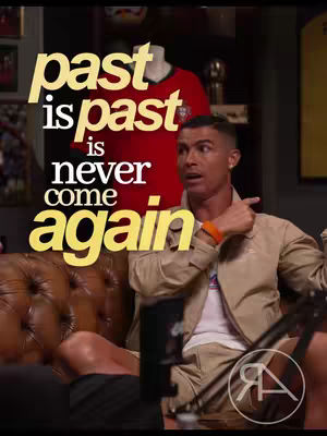 The image features Cristiano Ronaldo, seated on a brown leather couch, looking towards the right with a surprised expression and his right arm raised in a pointing gesture. Overlaid in a large, stylized font in yellow is the text "past is past is never come again," positioned prominently above Ronaldo and partially obscuring a red jersey on a mannequin in the background. The background is dimly lit.