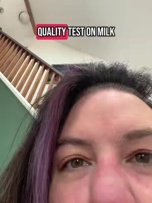A close-up shot focuses on the upper portion of a person's face, with the forehead and eyes prominently displayed. The person has dark hair with purple streaks on the left side, and the background shows a section of stairs leading upwards. A red rectangle overlay with white text that reads ''QUALITY TEST ON MILK'' is positioned above the person's head.
