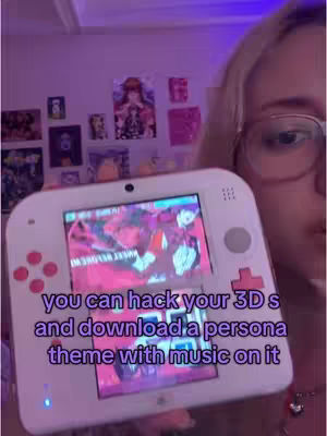 A selfie-style shot featuring a person holding a white 3DS console. The console screen displays colorful, animated graphics. The background is a room with posters on the wall, lit with a purple hue.
