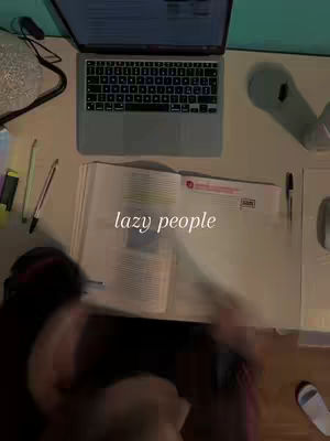An overhead shot of a desk with a laptop, an open textbook, and various study materials. The phrase 'lazy people' is overlaid on the open book in white font.