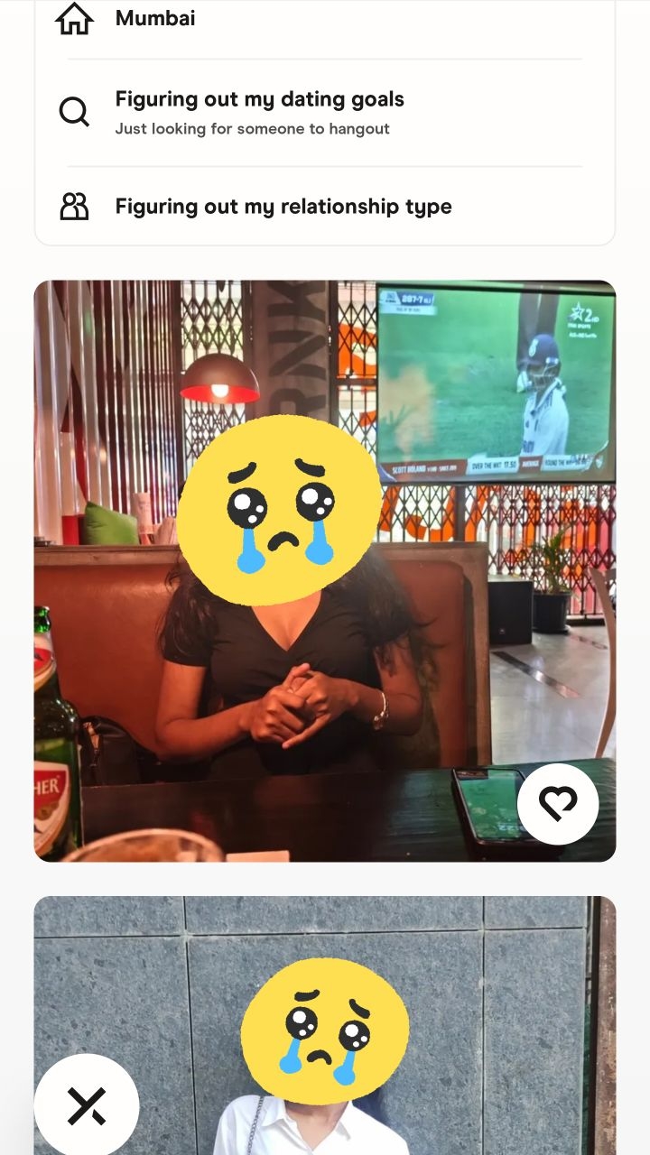 A cover image from the app Hinge features two parts: a top section with app settings (Mumbai location, "Figuring out my dating goals" and "Figuring out my relationship type"), and the bottom is a selfie inside a restaurant; the face is covered with a yellow crying face emoji, while a TV showing a cricket match is in the background.