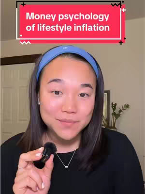 A woman in a black top with a blue headband is holding a small microphone, framed from the chest up. A text overlay reads "Money psychology of lifestyle inflation" in a red box. The background is neutral, with a door and a picture frame visible.
