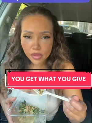 A woman with long, wavy brown hair is in the driver's seat of a vehicle, holding a clear plastic container with food and a fork. She is looking towards the camera with a slightly open mouth as if speaking. A text overlay reading "YOU GET WHAT YOU GIVE" is in a rectangle over her lower chest.