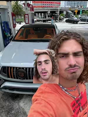 The image features a selfie-style shot of a man with a car at a gas station. The man is wearing an orange shirt and a silver chain, with a distressed expression. A smaller inset image of the man is also present. A silver luxury car is visible in the background, along with gas pumps and urban setting.