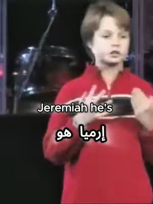 A young boy in a red shirt speaks into what appears to be a microphone, with text overlays in English and Arabic identifying him. The background is dark, suggesting a stage or studio setting.
