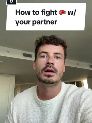 A man wearing a white sweater is in the foreground and looking at the camera with an open mouth suggesting he's speaking. Above him, a white bar with black text indicates the video topic.