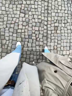 Top-down shot of feet walking on a cobblestone street. The feet are wearing blue jeans and white sneakers. The street is made of gray cobblestones. Text in white is placed in the middle of the image. 