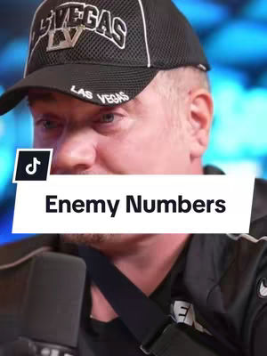 A man wearing a black cap with "LAS VEGAS" and a logo on it is in the foreground, his face partially visible. Overlayed on the image is a white rectangle with the text "Enemy Numbers" in bold black letters. The background is blurred, suggesting an interior setting with blue and white light.