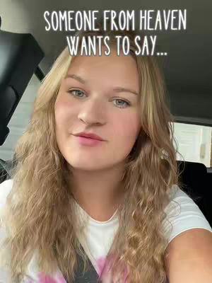 A woman is shown from the chest up, looking at the camera with a slight smile. She is in a car, with text overlayed at the top of the image in a white font, and wearing a white t-shirt. Her blonde hair is long and wavy.