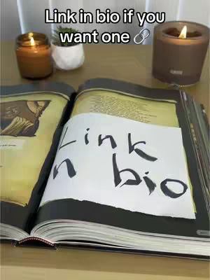 An open book with a handwritten note saying 'Link in bio' is displayed prominently. Two lit candles, a small potted plant, and a surface add to the setting.
