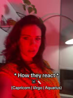 A woman with dark hair and an orange top is looking at the camera. The background is dark with the lighting being a strong red. Text overlay reads '* How they react *' and lists three zodiac signs.