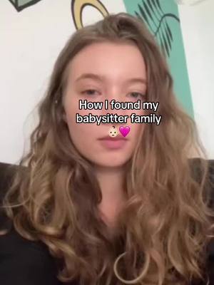 A young woman with long brown wavy hair looks directly at the camera. Text overlayed on image reads: "How I found my babysitter family". A baby face emoji and a pink heart emoji are present at the bottom of the text. The background is a white wall with a vertical patch of teal.