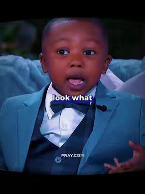 A young Black boy in a teal blazer and bow tie, looking upwards with an open mouth. Text overlay reads 'look what'. The background is slightly blurred. The logo of pray.com is at the bottom.