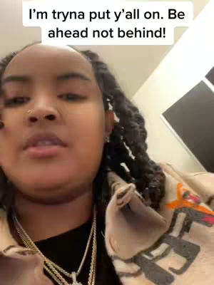 A selfie-style video cover image features a person of color with long, dark braids. The person is wearing a necklace and a patterned jacket against a nondescript indoor background. Text at the top states, "I'm tryna put y'all on. Be ahead not behind!"