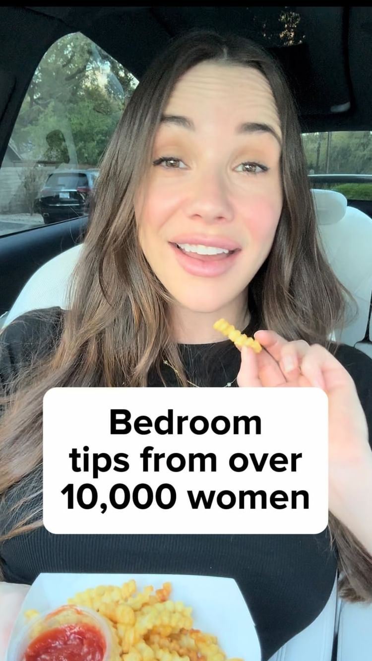 A woman with long brown hair smiles at the camera, holding a french fry. She appears to be in a car, with a cityscape blurred in the background. A white box overlay contains the text "Bedroom tips from over 10,000 women."