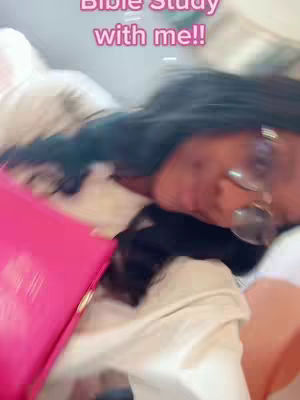 A person lies on a bed, holding a pink bible, the creator is in the frame with glasses on, the background is a white blanket. Text added in pink font overlaying the image.