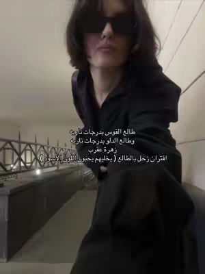 The cover image shows a person wearing sunglasses, captured in a selfie-style shot from the chest up, against a simple, lightly-colored interior background. Text in Arabic is overlaid on the image providing a list of astrological signs and their corresponding traits.