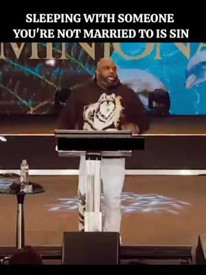 A man in a black hoodie is standing on a stage, speaking. The background is a blurred image of a large building or venue. Text overlayed is in black, it states "SLEEPING WITH SOMEONE YOU'RE NOT MARRIED TO IS SIN".