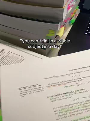 The image is a close-up of open textbooks and study materials on a desk, suggesting a study environment. The top section shows a stack of books with various sticky flags marking pages, and a part of a laptop is visible. The bottom section shows an open textbook page with printed text and a highlighter mark. The color palette is muted, with white, grey, and various colors used to create contrast.