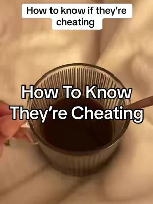 A close-up shot features a glass cup filled with a dark liquid, possibly coffee or tea. The cup stands on a light-colored surface, and a spoon rests against its rim. Above the cup, a text overlay reads 'How to know if they're cheating'. The background appears to be a soft, blurred fabric. The composition is simple, focusing attention on the central message.