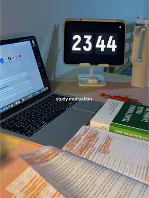 The cover image showcases a well-lit desk setup, ideal for studying. A laptop is open, displaying a document on its screen alongside open books filled with annotations. A digital clock in the center displays the time '23:44'. Additional items include a red pen and a tall, white, cylindrical object likely a water container, all against a neutral backdrop.