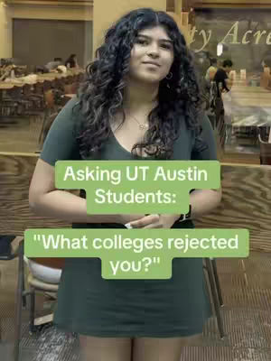 A young woman stands in a casual setting, likely a public space. She is centered in the frame, wearing a dark green top and skirt, with long, dark, curly hair. The image is well-lit, with some background elements including tables and what appears to be information on a sign. Green text boxes provide context: 'Asking UT Austin Students:' and "What colleges rejected you?"