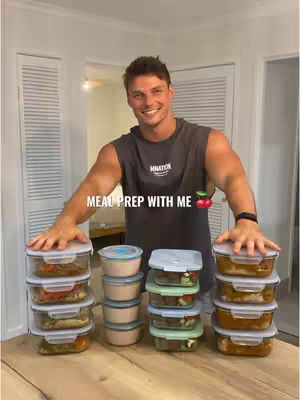 A man is standing behind a table with pre-packaged meals. He is smiling and has his hands resting on top of the containers. The image is brightly lit, with a clean kitchen in the background.