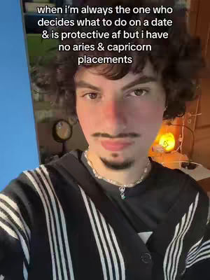 A selfie of a young man with curly brown hair, a trimmed mustache and goatee, and a small chain necklace. He is wearing a black and white striped button-down shirt with a black t-shirt underneath. Text overlay on the image.