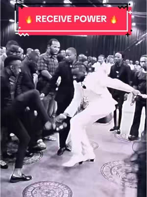 The image captures a dynamic indoor scene with a group of people, primarily men, interacting. Dominating the frame is a man in a white suit, actively engaging with others, possibly dancing or in a moment of performance. Additional individuals, some in suits, are positioned in the background, forming a crowd. The overall composition is slightly chaotic, highlighted by the movement and expressions of the figures. The setting appears to be an event space.