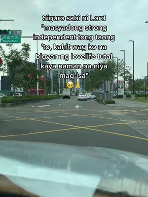 The image shows a road scene from what appears to be inside a car looking out. There is text overlaid at the top, the road is in the foreground with multiple lanes and dividers. Buildings in the background with trees.