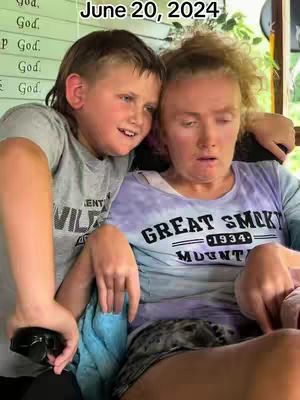 A cover image showing a young boy and an adult woman, likely his mother, in a close embrace. The boy is on the left, partially obscuring the woman, and has his arm around her. Both are looking partly away, suggesting a moment of shared emotion. The boy wears a grey t-shirt, and the woman wears a tie-dye t-shirt. Text in the upper left corner of the image indicates the date.