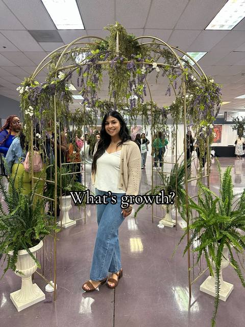 A woman stands inside a decorative metallic archway adorned with greenery and flowers. She is smiling at the camera, with other people visible in the background within a brightly lit room. The words 'What's growth?' appear over the image.