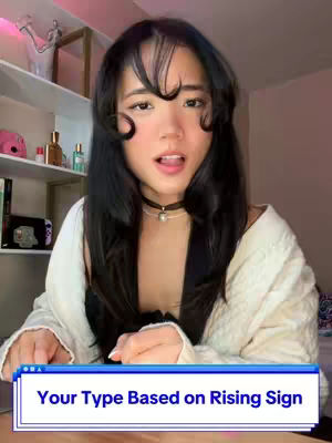 A woman with long dark hair, wearing a black top, a white sweater, and a choker. She has her mouth open and is looking towards the camera, with a text overlay in the bottom.