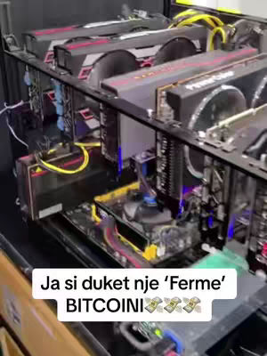 The image shows a close-up view of a cryptocurrency mining setup. Several high-end graphics cards are installed in a metal frame. The cards are black and red, with prominent fans and cooling elements. Cables and wires connect the components, and blue and yellow lights illuminate the setup. A text overlay at the bottom reads "Ja si duket nje 'Ferme' BITCOINI" with money bag emojis.