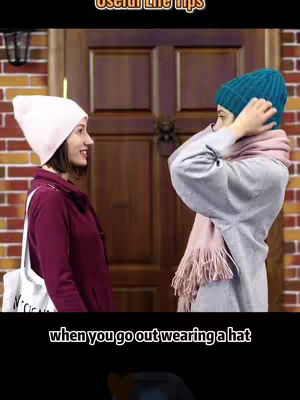 Two young women are standing in front of a doorway. One is adjusting their knit cap, wearing a light purple jacket and a teal winter hat. The other has a pink knit cap, maroon jacket, and a white tote bag. The background consists of a brick wall and a wooden door.