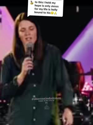 A woman with long brown hair is holding a microphone and singing, against a blurred background. The image on the top left features a text bubble with a message, and at the bottom, there is a handle and a small logo.