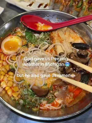 A close-up shot of a bowl of ramen. The bowl is silver with a red spoon resting inside. The ramen is filled with various ingredients, including noodles, an egg, vegetables, and broth. The text overlay is white.
